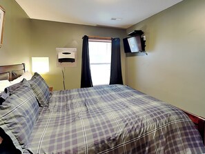 Una habitación de hotel con cama, televisor montado en la pared, ventana con cortinas y ventilador de techo.