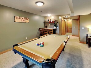 Una mesa de billar con bolas, un cartel que dice "Deep Creek Lake" y una zona de cocina con sillas y una mesa.