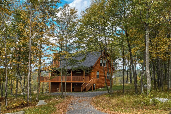 A wooden cabin with a deck, surrounded by trees and a gravel path. - Mountain Dreams by Taylor Made Deep Creek (McHenry)