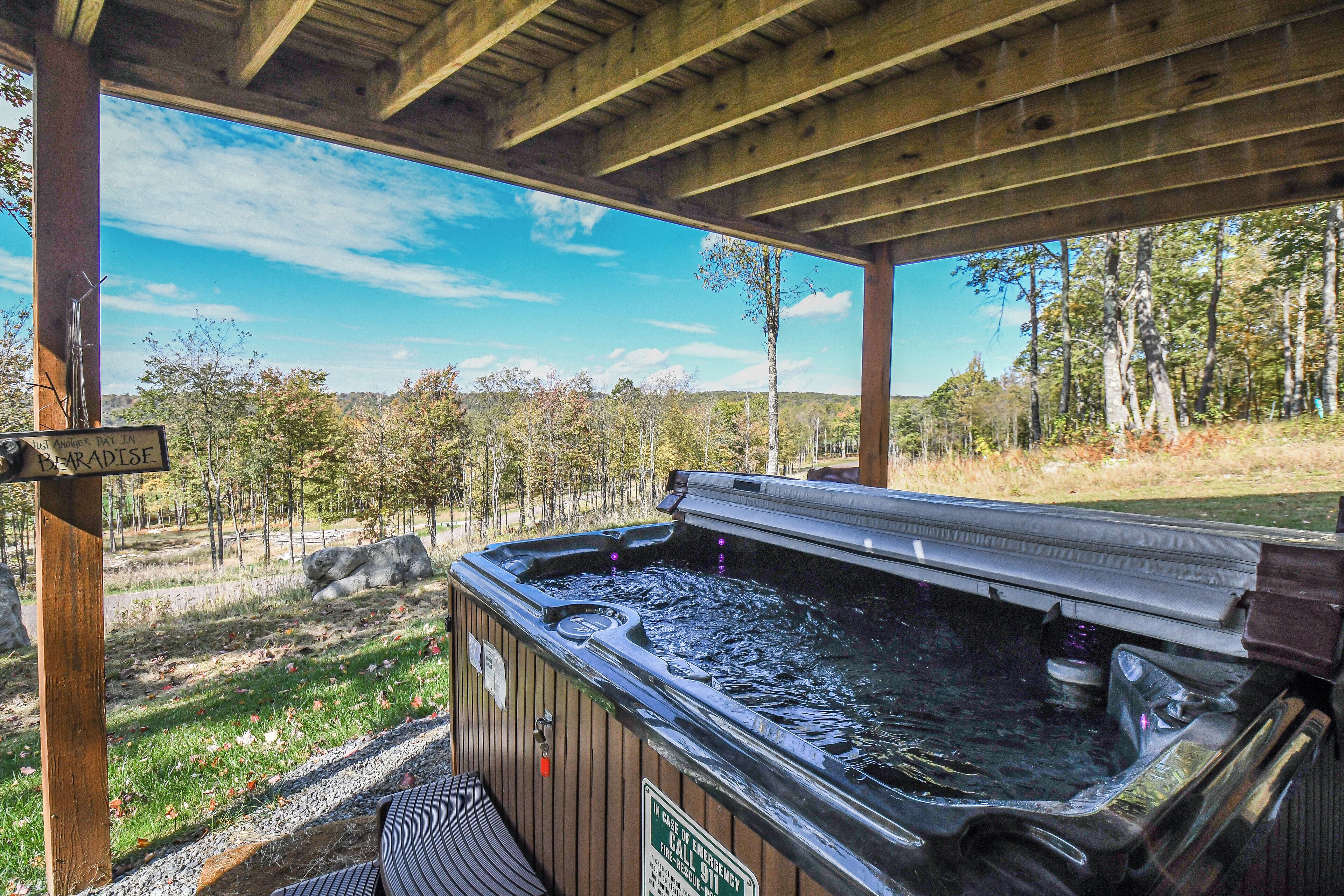 A hot tub under a wooden pergola with a view of a forested area.