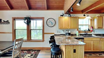 A kitchen with wooden cabinets, a marble countertop, a coffee maker, and a window with a view of trees.