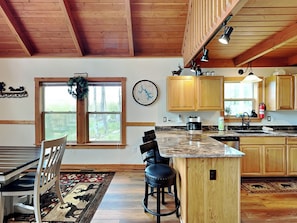 A kitchen with wooden cabinets, a marble countertop, a coffee maker, and a window with a view of trees. - Mountain Dreams by Taylor Made Deep Creek (McHenry)