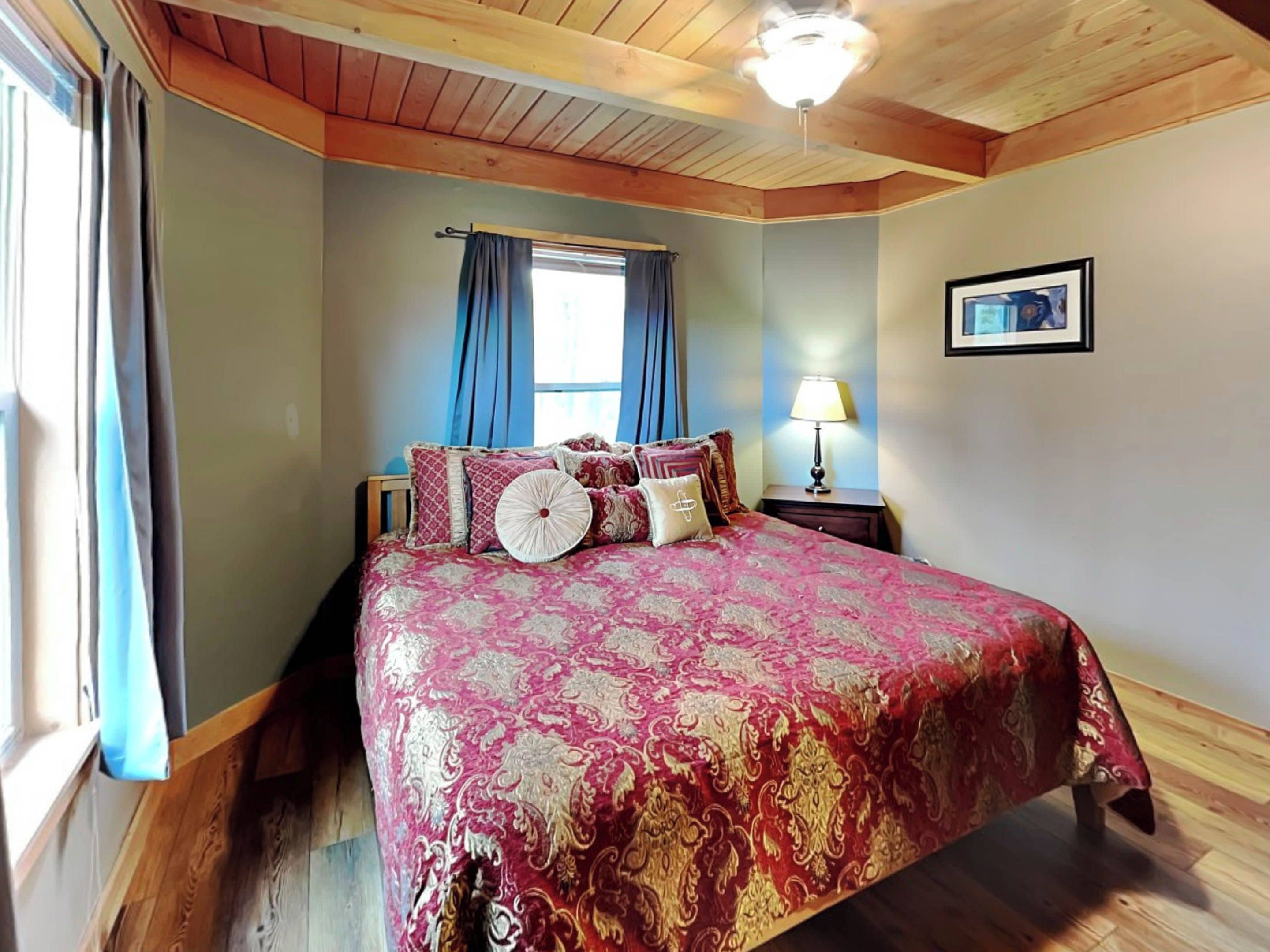 Een slaapkamer met een groot bed, houten plafond en een raam met gordijnen.