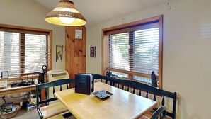 A dining area with a wooden table and benches, a hanging light fixture, and windows with blinds. - Mountain Escape by Taylor Made Deep Creek (McHenry)