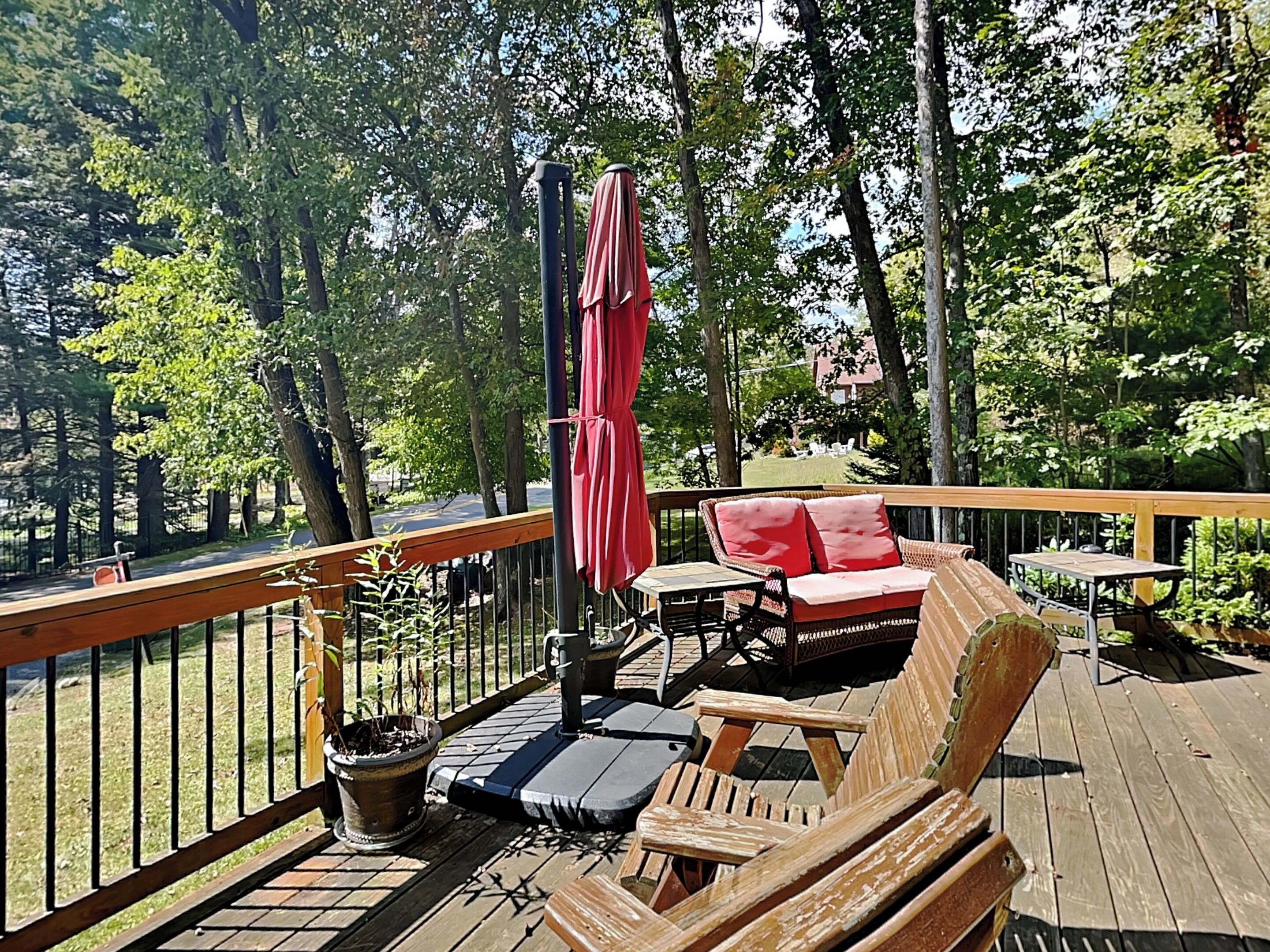 A wooden deck with outdoor furniture, including a red umbrella and a wicker sofa.