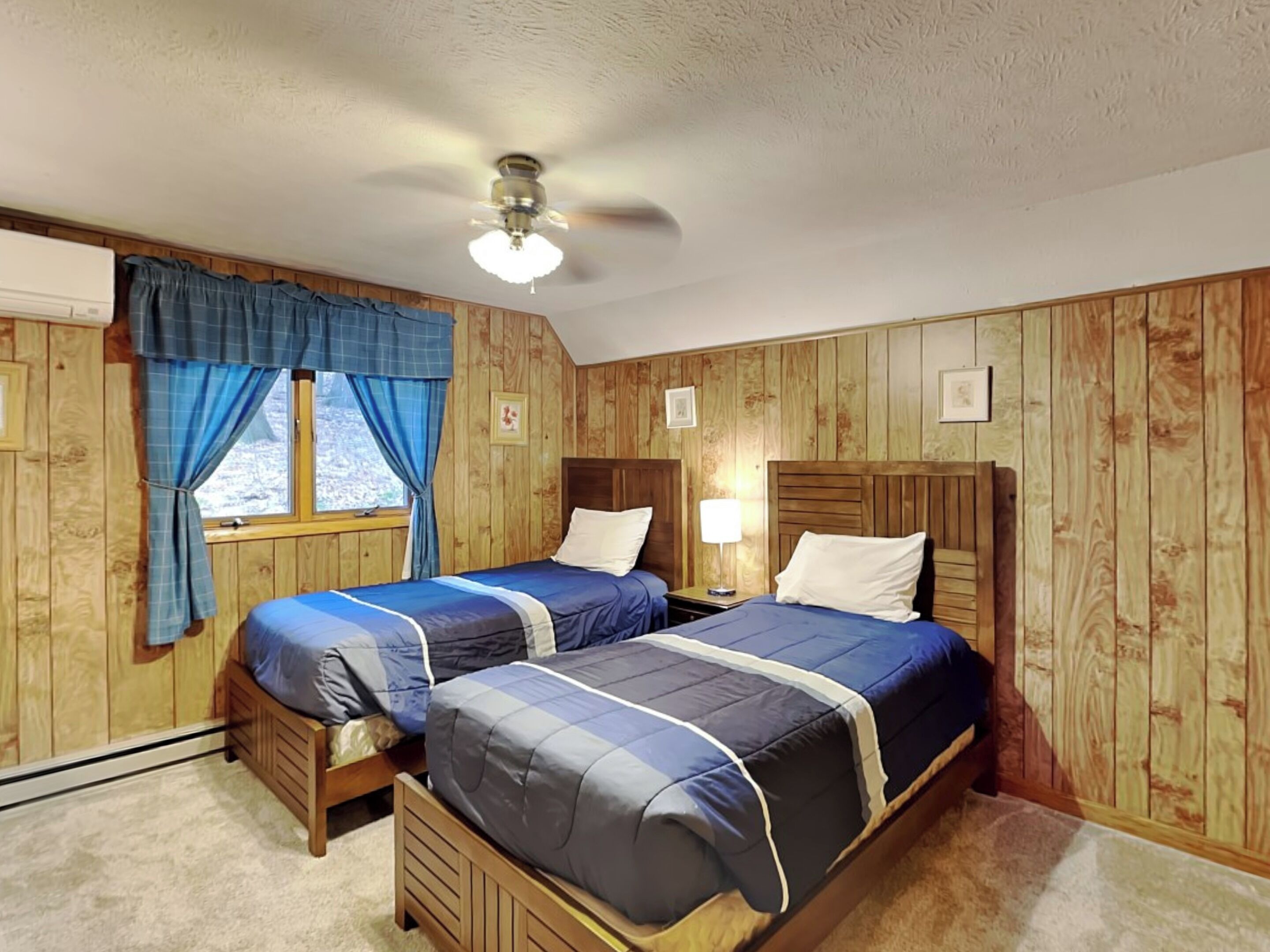A room with two wooden beds, a ceiling fan, and a window with curtains.