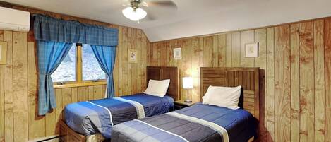 A room with two wooden beds, a ceiling fan, and a window with curtains.