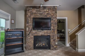A living room with a stone fireplace, a mounted television, and a fish display. - Mountain Splendor by Taylor Made Deep Creek (Swanton)