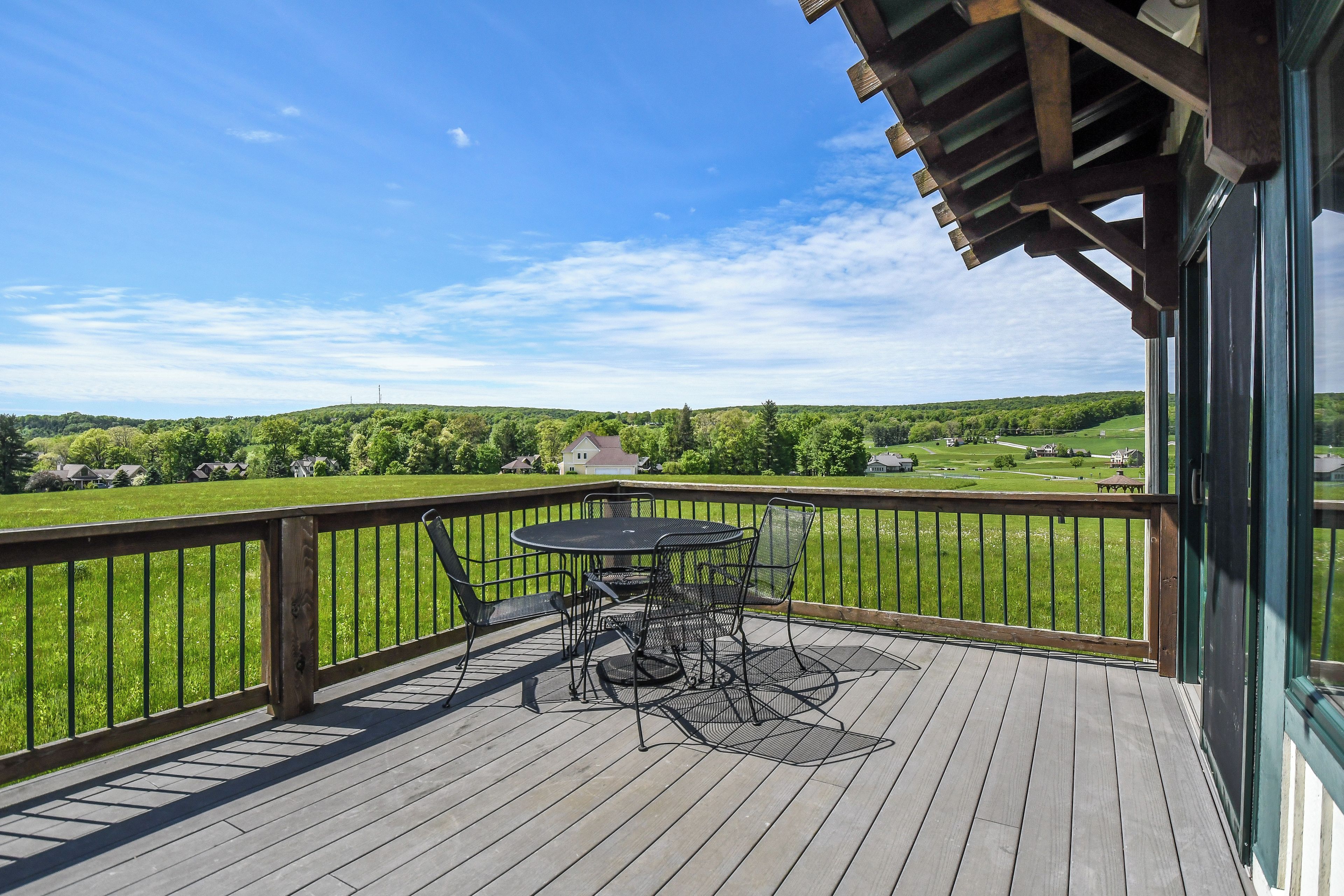 Une terrasse en bois avec une table et des chaises, donnant sur un paysage verdoyant.