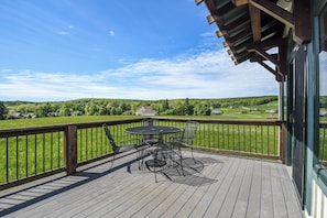 A wooden deck with a table and chairs, overlooking a green landscape. - Mountain Splendor by Taylor Made Deep Creek (Swanton)