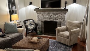 A living room with a fireplace, a television mounted above it, and two patterned armchairs. -  BRAND NEW KITCHEN! CLOSE TO DOWNTOWN EDGARTOWN AND THE BEACH! (Edgartown)