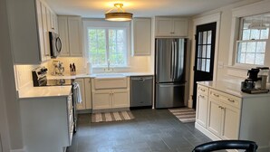 A modern kitchen with white cabinets, stainless steel appliances, and a black door. -  BRAND NEW KITCHEN! CLOSE TO DOWNTOWN EDGARTOWN AND THE BEACH! (Edgartown)