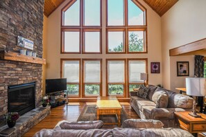 Amplia sala de estar con chimenea de piedra, ventanas grandes, un sofá cómodo y un televisor de pantalla plana.