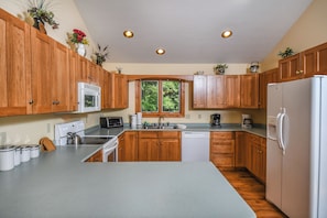 A kitchen with wooden cabinets, a stainless steel refrigerator, a microwave, a stove, and a window with a view of greenery. - Mountain Top Lodge by Taylor Made Deep Creek (McHenry)