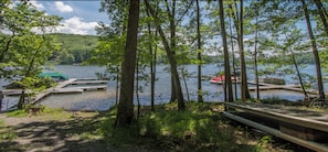 A lakeside view with docked boats, a wooden bench, and a forested area.