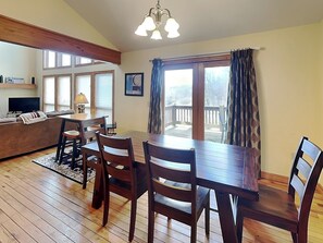 A cozy living room with a wooden floor, a dining table with chairs, a sofa, a TV, and a balcony with a railing.