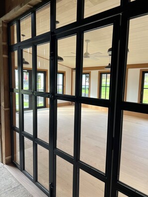 A room with large windows, a ceiling fan, and a view of the outdoors. - French Woods Farmhouse: Catskills | 12 Acres | Private Pond | Hot Tub | Firepit (Hancock)