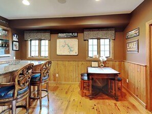 A kitchen with wooden paneling, a bar area with stools, a map on the wall, and a sign indicating 'Lake'. - Mountainlair by Taylor Made Deep Creek (McHenry)
