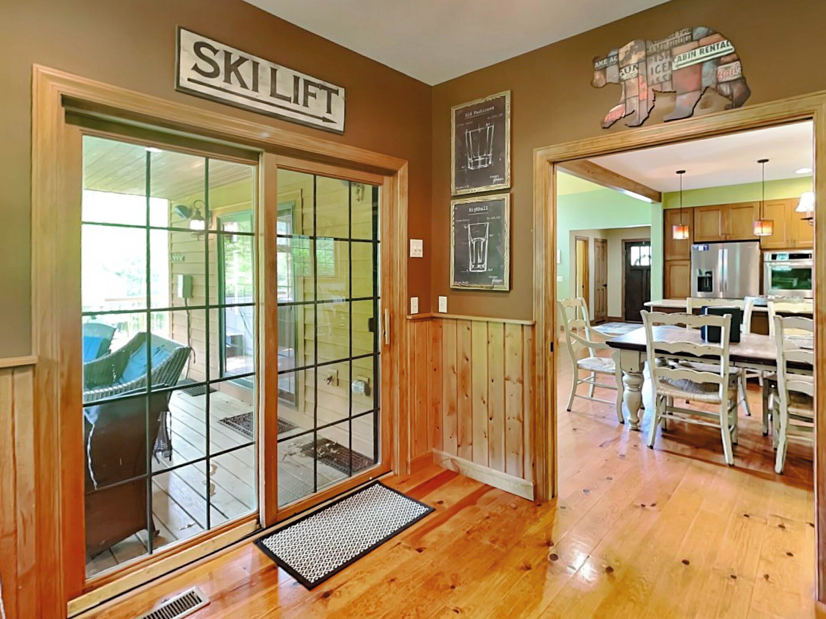 A wooden interior with a ski lift sign, a dining area with white chairs, and a kitchen with wooden cabinets.