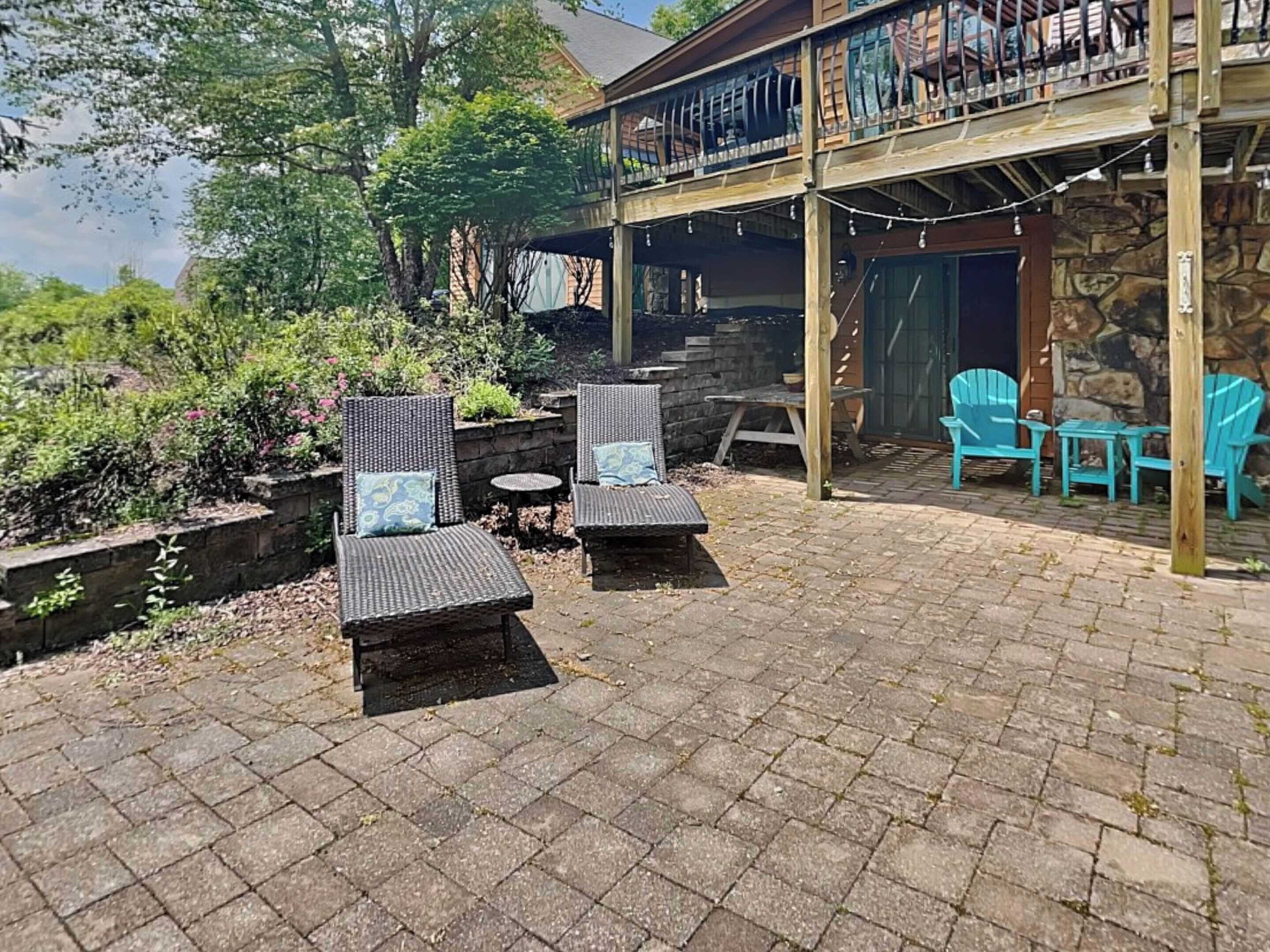 A patio area with wicker chairs and a table, a stone wall, and a wooden deck with chairs.