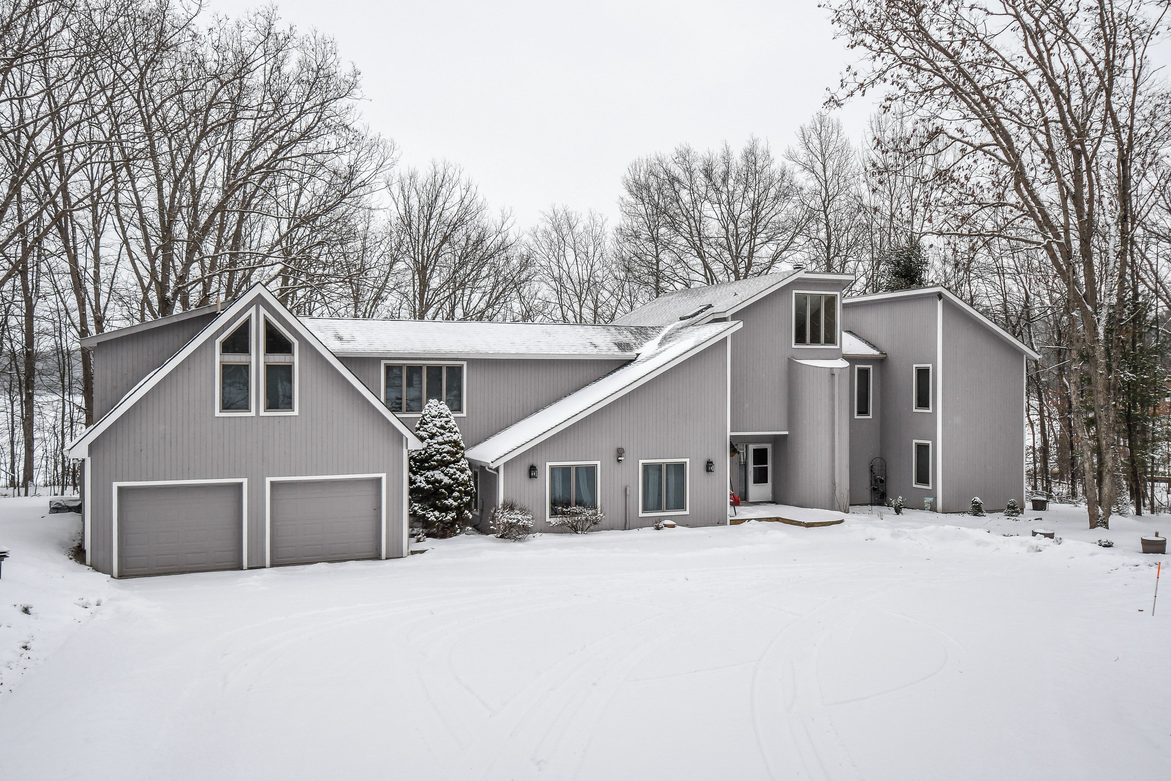 A two-story house with a garage, a covered porch, and a snow-covered yard.