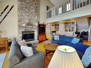 A spacious living room with a stone fireplace, a blue sofa, a wooden coffee table, and a TV.