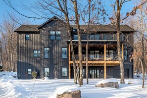 Un immeuble moderne à plusieurs étages, doté d’une façade sombre, de grandes fenêtres et d’un balcon en bois.