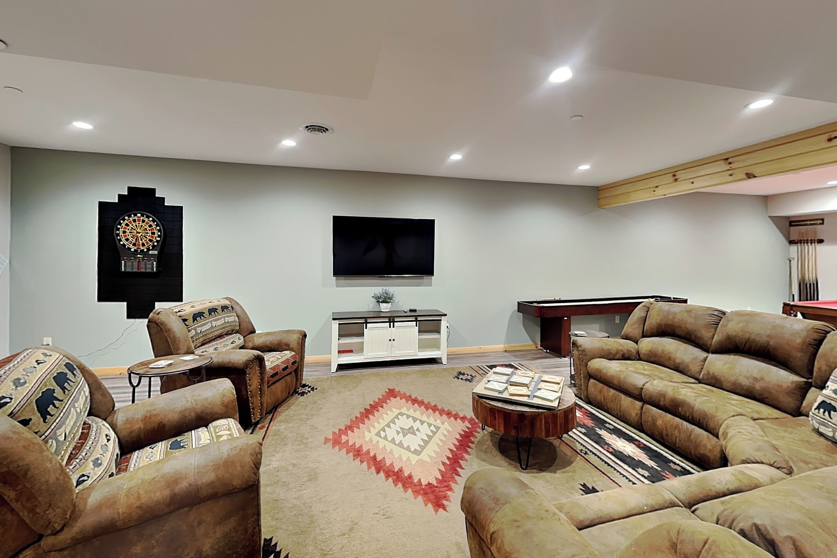 A living room with leather sofas, a dartboard, a flat-screen TV, a pool table, and a patterned rug.