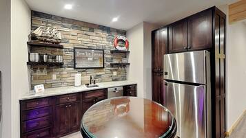 A kitchen with dark wooden cabinets, a stainless steel refrigerator, a stone backsplash, and a glass-top table.
