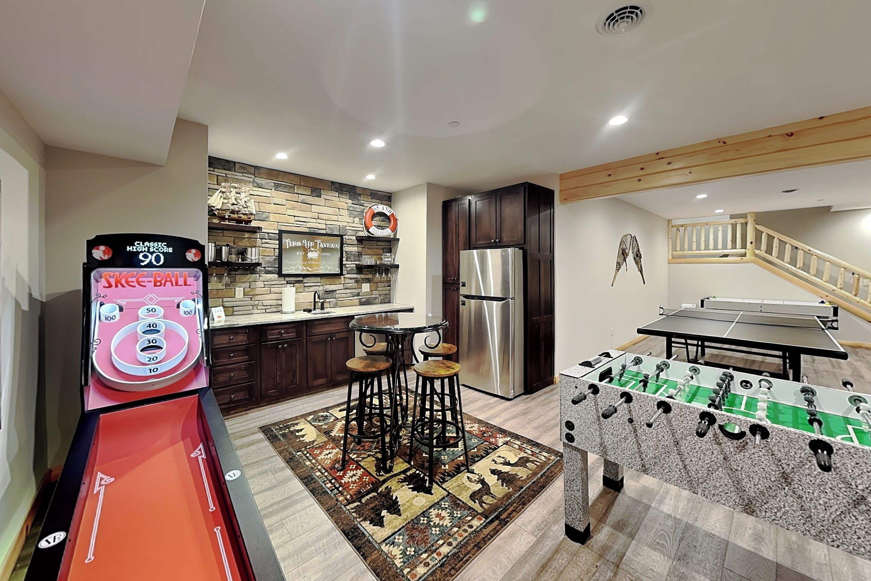 A kitchen with a foosball table, a foosball table with a score of 90, and a bar area with stools.