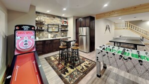 Uma cozinha com mesa de futebol de mesa, mesa de futebol de mesa com placar de 90, e área de bar com banquetas.