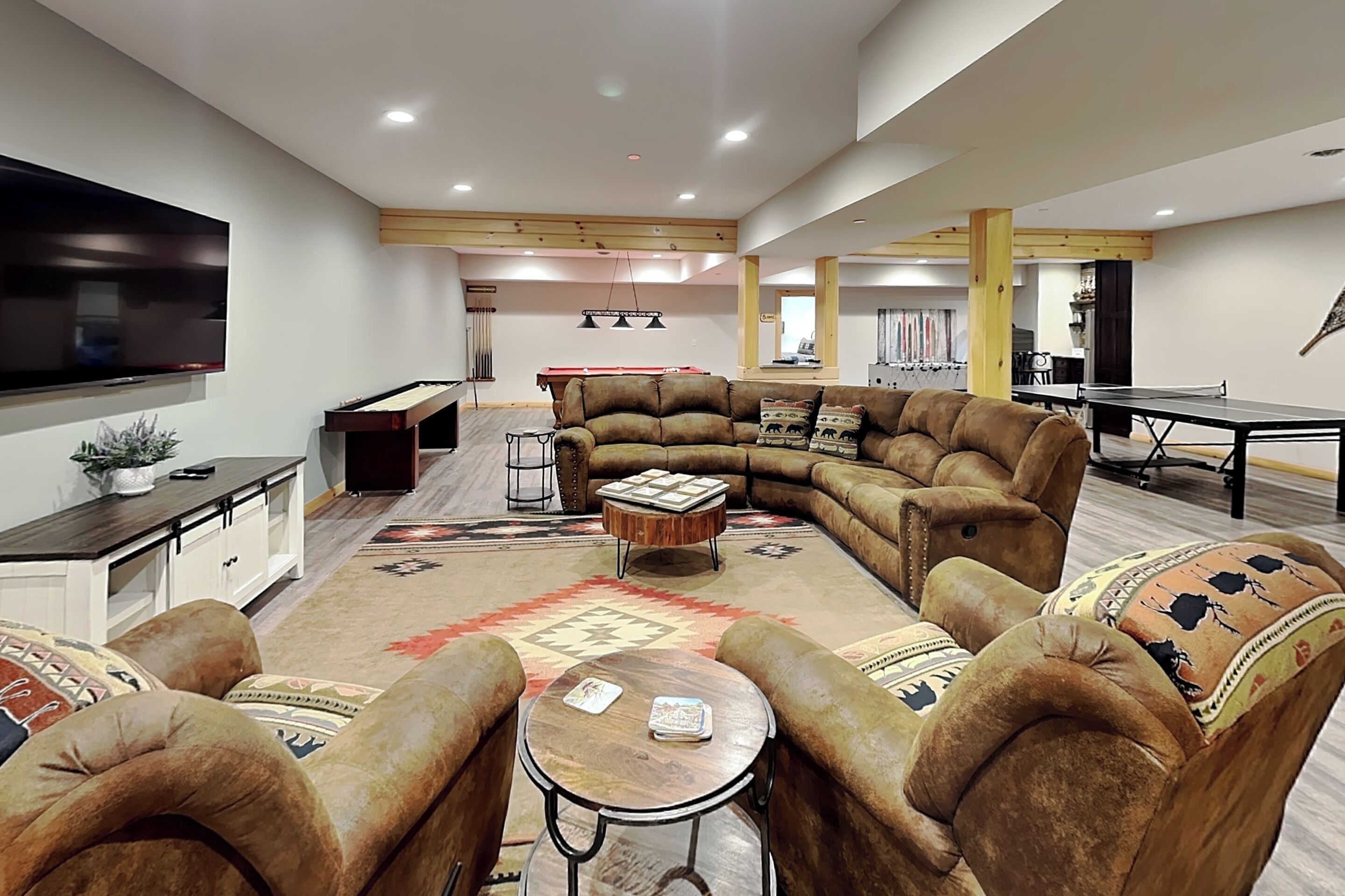A spacious living area with a large sectional sofa, a coffee table, and a flat-screen TV mounted on the wall.