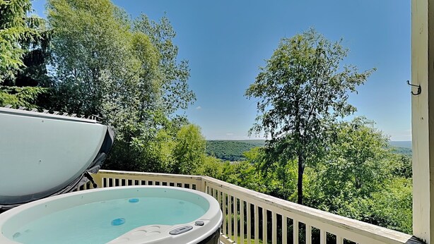 A hot tub on a deck with a view of a forested landscape.