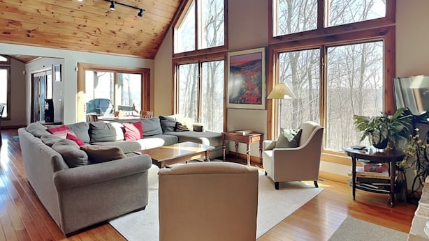 A spacious living room with a high ceiling, large windows, a sectional sofa, a small table, and a chair. - One Ski Hill by Taylor Made Deep Creek (McHenry)