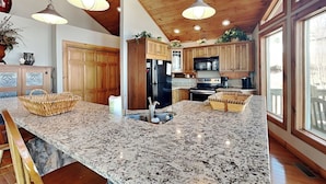 A spacious kitchen with granite countertops, wooden cabinets, and a central island with bar stools. - One Ski Hill by Taylor Made Deep Creek (McHenry)