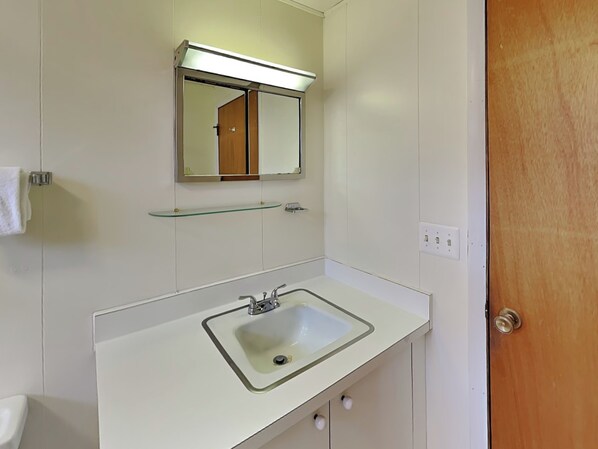 A bathroom with a white sink, a mirror above it, and a glass shelf. - Our Golden Retreat by Taylor Made Deep Creek (Swanton)