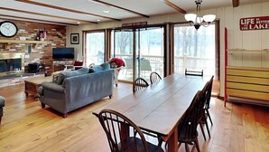 A spacious living room with a large wooden dining table, a grey sofa, and a fireplace. - Our Golden Retreat by Taylor Made Deep Creek (Swanton)