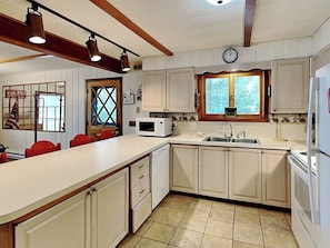 A kitchen with white cabinets, a microwave, a sink, and a clock on the wall.
