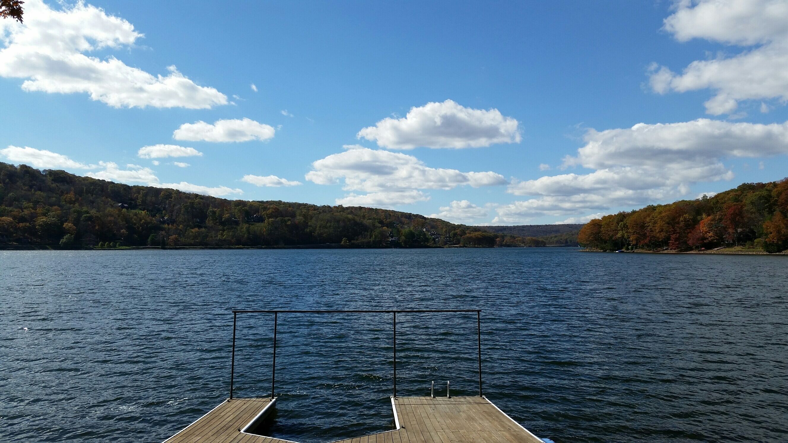 A wooden dock extending into a calm lake with a forested hillside in the background.