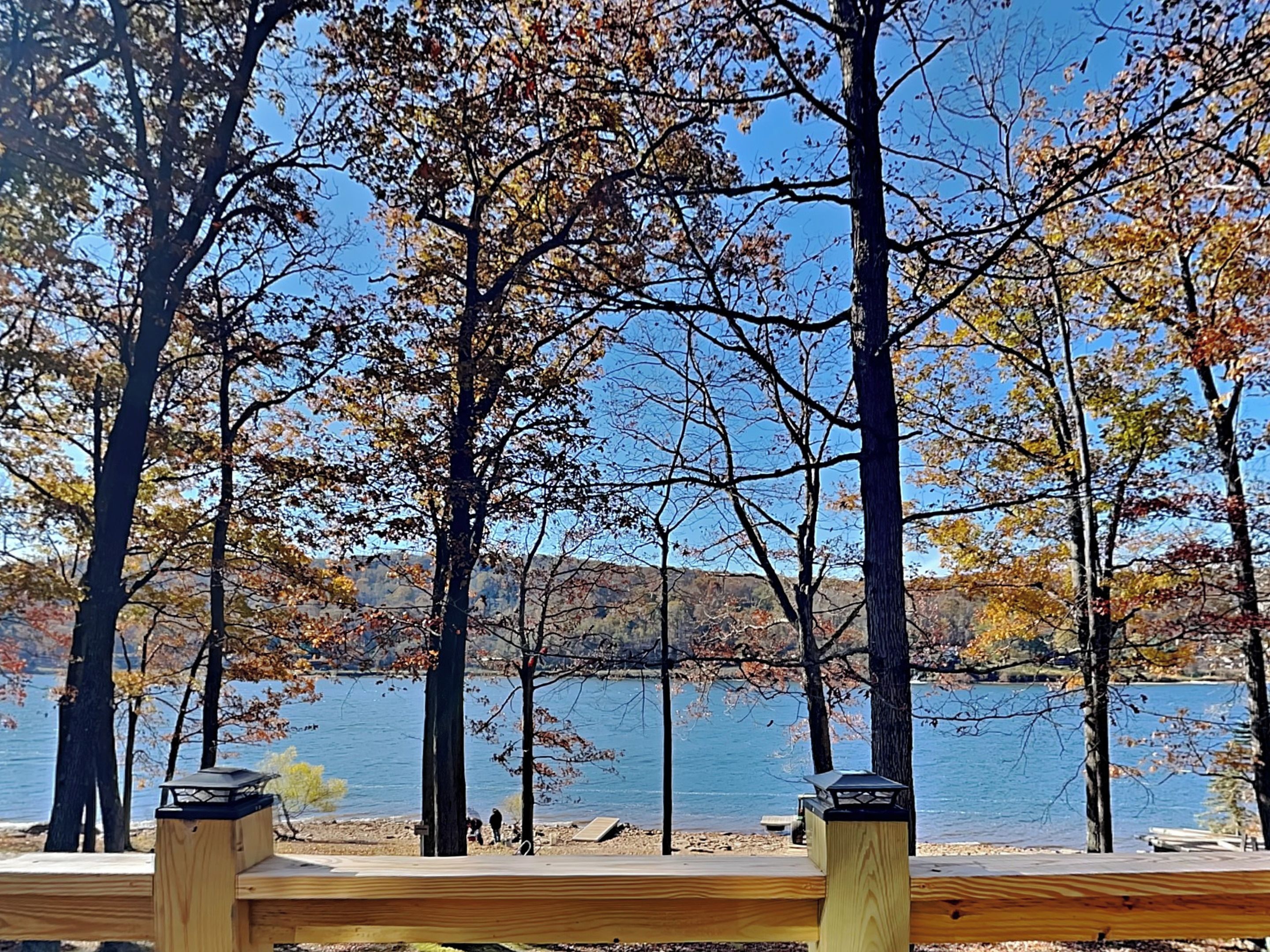 A wooden deck overlooking a lake with autumn-colored trees and a clear sky.