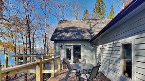 Une terrasse en bois avec une table et des chaises, donnant sur une étendue d’eau et des arbres.