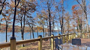 Une terrasse en bois avec une balustrade donnant sur un lac, entourée d’arbres aux feuilles d’automne.