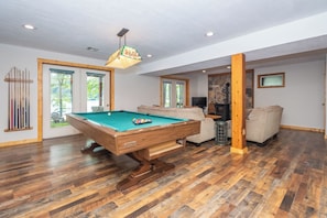 A pool table in a room with wooden flooring and a stone accent wall. - Over the Rainbow by Taylor Made Deep Creek (McHenry)