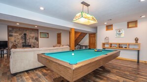 Une table de billard dans une pièce avec un mur en pierre, des poutres en bois et un luminaire suspendu.