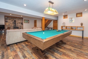 A pool table in a room with a stone wall, wooden beams, and a hanging light fixture. - Over the Rainbow by Taylor Made Deep Creek (McHenry)