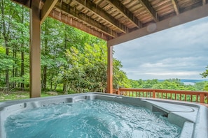 Relax in a serene hot tub surrounded by lush greenery and trees, accessible via a wooden deck.