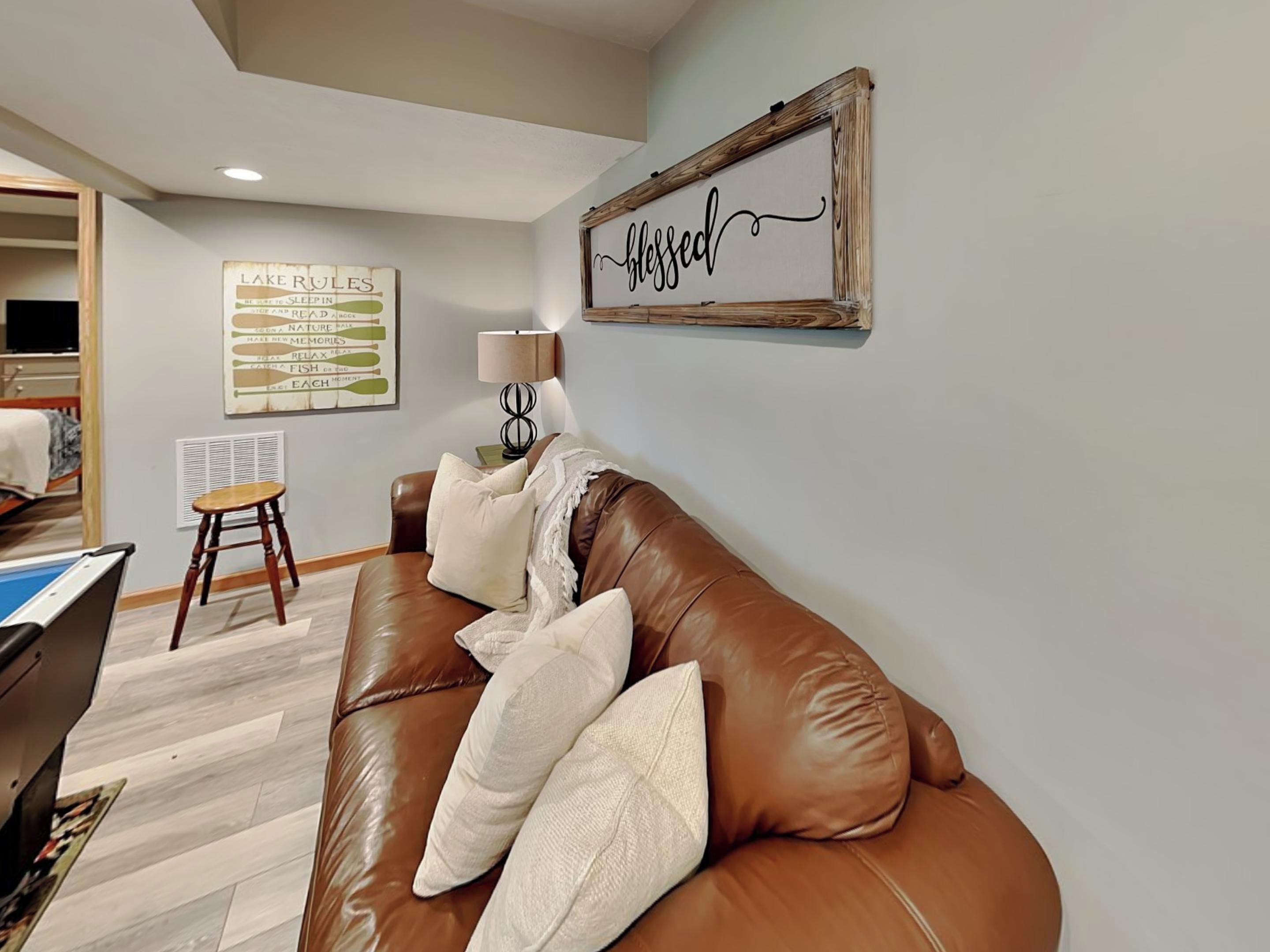 A cozy living room with a brown leather couch, a small wooden stool, and a wall-mounted lamp.