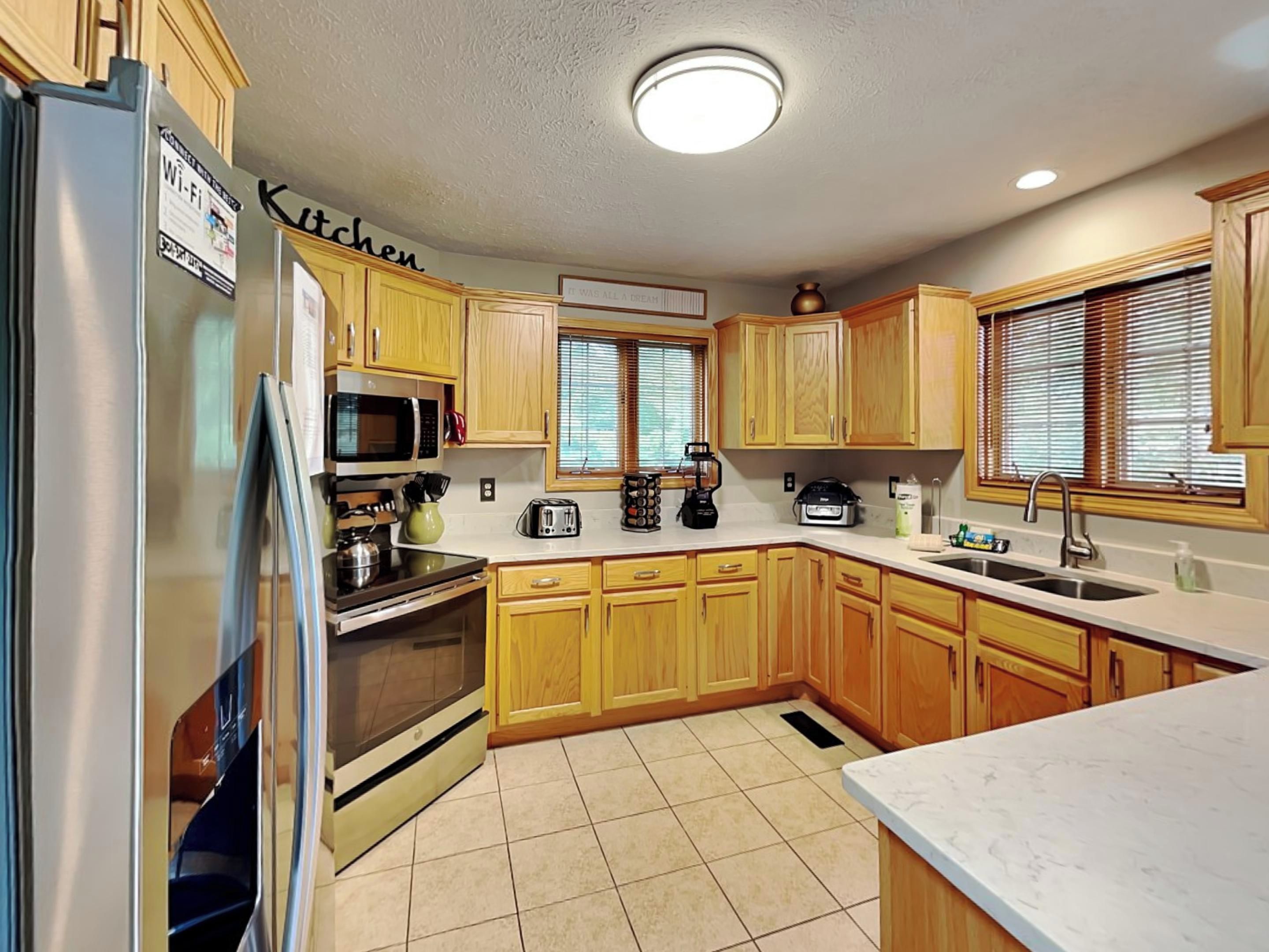 A kitchen with wooden cabinets, a refrigerator, a microwave, a stove, a toaster, and a sink.