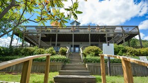 A wooden staircase leading to a covered deck with railings, surrounded by greenery.
