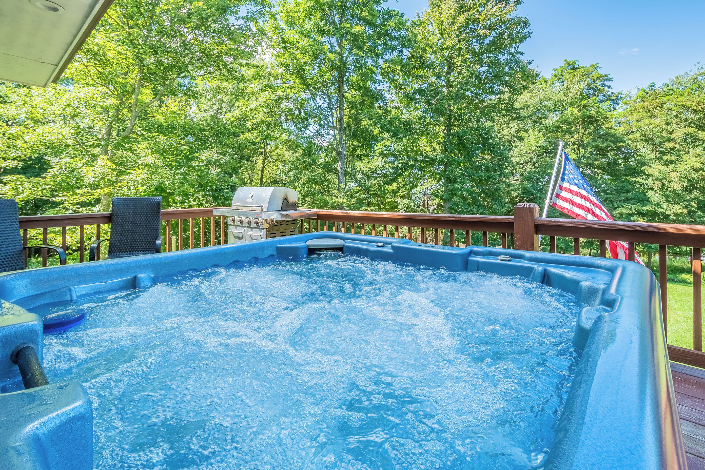 Un bain à remous sur une terrasse en bois, avec un barbecue et un drapeau américain.